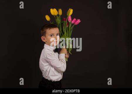 Der Junge mit Vitiligo in einem weißen Hemd und ein Fliege mit Tulpen auf schwarzem Studio-Hintergrund Stockfoto