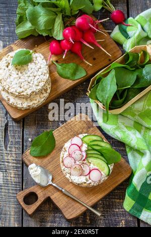 Gesundes Frühstück. Knusprige Knäckebrot-Sandwiches mit Ricotta, Rettich und frischer Gurke auf einem Holztisch. Stockfoto