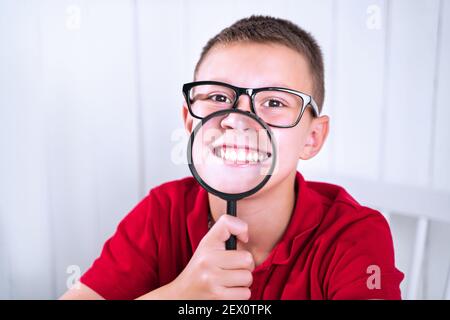 Kleiner Schuljunge drückt positive und negative Emotionen durch eine Lupe aus. Geht zurück zur Schule. Erziehen, wie man Gefühle ausdrücken kann. Stockfoto