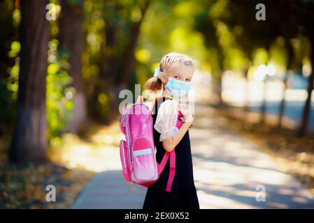 Schulmädchen tragen Maske und Rucksack vor Coronavirus zu schützen. Kind, das nach einer Pandemie zur Schule geht. Stockfoto