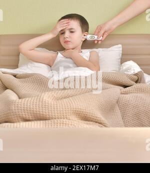 Ein krankes Kind liegt im Bett. Messung der erhöhten Temperatur mit einem Ohrthermometer. Stockfoto