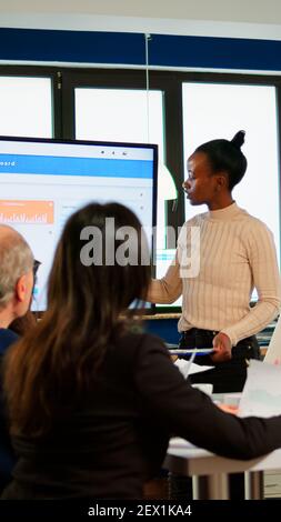 Afrikanischer Projektmanager, der ein Finanzmeeting mit statistischen Grafiken und Diagrammen auf einem interaktiven Whiteboard-Touchscreen-Gerät abhält. Executive Director arbeitet im Broadroom der Kreativagentur. Stockfoto