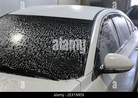 Weißes modernes Auto mit Schaum in der Autowäsche bedeckt Stockfoto