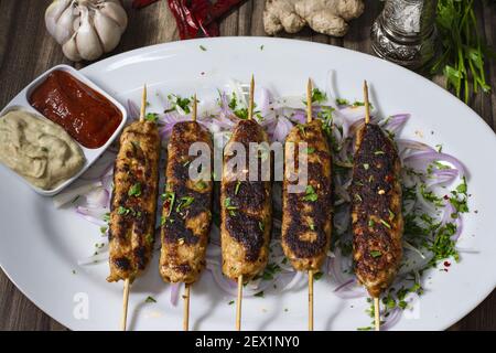 Hausgemachte appetitliche Hähnchen-Kababs mit Spiessen auf einem Oval serviert Teller mit Sauce Stockfoto