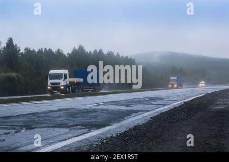 Lastwagen mit Containern fahren im Nebel entlang des Landes Straße Stockfoto