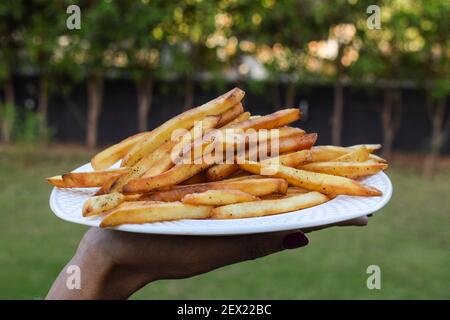 Weibchen hält einen Teller mit knusprig knusprigen Pommes frites Haufen. Kartoffelchips mit würzender Masala. Sehr lecker beliebte Teezeit Snack Artikel weltweit Stockfoto