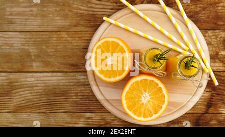 Orangensaft in Glasflaschen. Der Saft ist mit einem Zweig Rosmarin verziert. Saft auf Holzhintergrund. Draufsicht Stockfoto