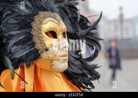 Venezianische Maskenmaske, Karnevalsmaske zum Verkauf in Venedig, Italien. Knisternde Gesichtsmaske aus Porzellan, umgeben von einer Wolke aus schwarzen Federn Stockfoto
