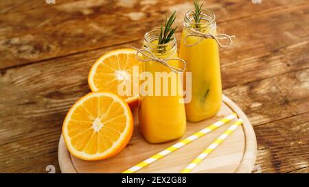 Orangensaft in Glasflaschen. Der Saft ist mit einem Zweig Rosmarin verziert. Saft auf Holzhintergrund Stockfoto