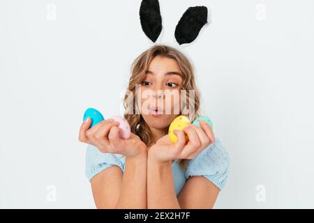 Überrascht schöne junge Frau hält Blick auf Ostereier und trägt Hasenohren steht auf weißem Studio Hintergrund. Stockfoto