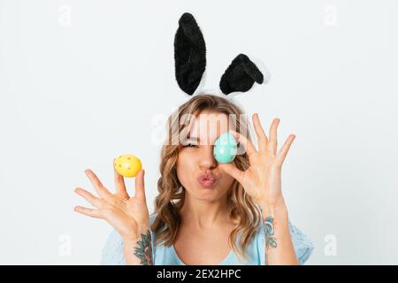 Festliche Stimmung, junge Frau trägt Osterhasen Ohren Spaß mit farbigen Eiern in der Nähe ihrer Augen auf weißem Hintergrund halten. Stockfoto