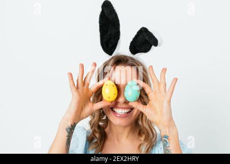 Portrait glücklich junge Frau trägt Hase Ohren Ostern feiern Spaß mit bunten Eiern vor den Augen auf weißem Hintergrund halten. Stockfoto