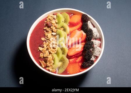 SCHWARZE TRAUBEN, ERDBEERE UND FEIGEN SMOOTHIE MIT DRACHENFRUCHT, KIWI, ERDBEERE, MAULBEERE UND CRANBERRY-MANDEL-MÜSLI GEKRÖNT Stockfoto