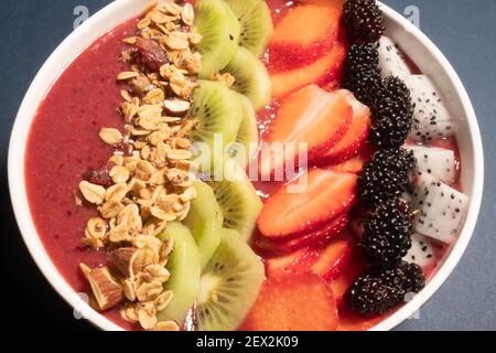 SCHWARZE TRAUBEN, ERDBEERE UND FEIGEN SMOOTHIE MIT DRACHENFRUCHT, KIWI, ERDBEERE, MAULBEERE UND CRANBERRY-MANDEL-MÜSLI GEKRÖNT Stockfoto