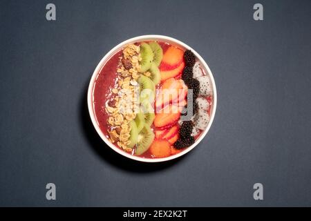 SCHWARZE TRAUBEN, ERDBEERE UND FEIGEN SMOOTHIE MIT DRACHENFRUCHT, KIWI, ERDBEERE, MAULBEERE UND CRANBERRY-MANDEL-MÜSLI GEKRÖNT Stockfoto