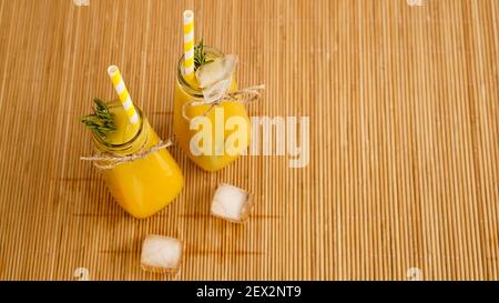 Orangensaftflaschen und Papierhalme. Eisiger Drink an einem sonnigen Tag. Eisstücke in einer Flasche und auf einer Bambusserviette Stockfoto