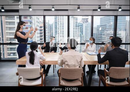 Gruppe von multiethnischen Geschäftsleuten, die Gesichtsmaske mit Daumen tragen Während des Meetings in die Geschäftsvereinbarung treffen und zustimmen Neues normales Büro während Stockfoto