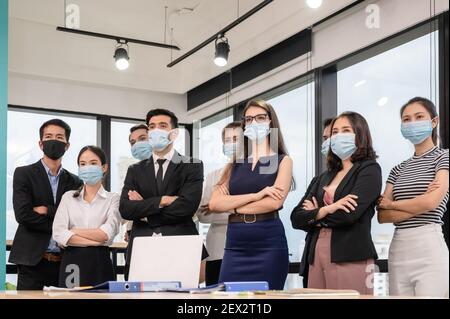 Multiethnisches, selbstbewusstes Geschäftsteam, das mit gekreuzten Armen steht und trägt Medizinische Maske im modernen Büro im Geschäftsviertel Stockfoto