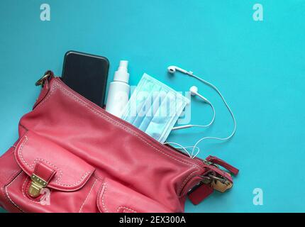 Frau rote Handtasche mit Gesichtsmaske, Handdesinfektionsmittel, Ohrhörer und Smartphone. Draufsicht. Stockfoto