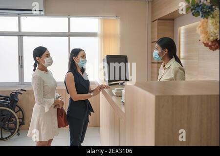 Patienten mit Gesichtsmaske Kontakt für Behandlung Krankheit mit Rezeptionist An der Rezeption im Krankenhaus Stockfoto