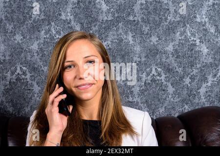 Porträt einer blonden jungen europäischen Geschäftsfrau, die am Telefon spricht und in die Kamera schaut Stockfoto