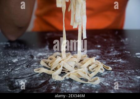 Zubereitung hausgemachter Fettuccine auf einer hölzernen maza. Traditionelles Schneidekonzept der italienischen Küche, Schneiden roher Teig in Tagliatelle auf Kopierraum Stockfoto