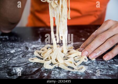 Zubereitung hausgemachter Fettuccine auf einer hölzernen maza. Traditionelles Schneidekonzept der italienischen Küche, Schneiden roher Teig in Tagliatelle auf Kopierraum Stockfoto