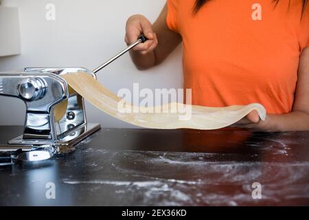 Zubereitung von hausgemachter Fettuccine auf der Pasta-Maschine. Schneiden roher Teig in Tagliatelle auf spezielle Ausrüstung, traditionelle italienische Küche Konzept, Kopie Spa Stockfoto