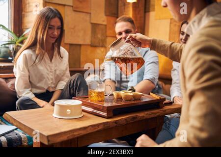 Junger Mann gießt Tee in Glas Tasse im Café Stockfoto