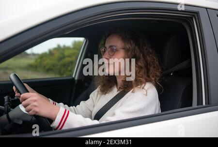 Junge Frau fährt ein Auto, Konzept der neuen Fahrer. Die Frau hat lockiges blondes Haar. Stockfoto