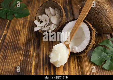 Kokosöl im Holzlöffel und Kokosnuss-Chips auf dem braunen Holzhintergrund. Naturprodukte. Stockfoto