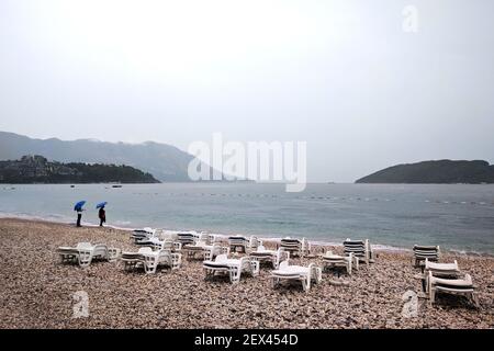 Herbstregen auf einem einsamen Strand in der Nähe der Adria. Menschen unter Sonnenschirmen. September in Montenegro. Stockfoto