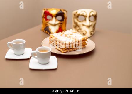 Typische italienische Karnevalsfritter (Chiacchiere di Carnevale) mit Puderpulver bestäubt. Zusammensetzung mit zwei Tassen Kaffee und im Hintergrund sind Venet Stockfoto