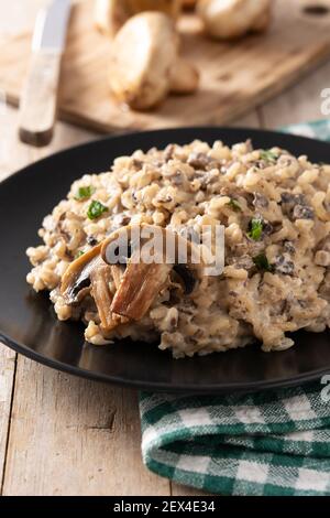 Risotto mit Pilzen auf schwarzem Teller auf Holztisch. Stockfoto