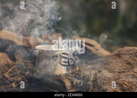 Eisenkrug am Lagerfeuer, in Rauch auf dem Campingplatz im Wald Stockfoto