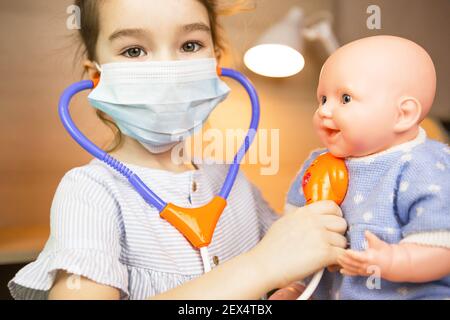 Ein Mädchen mit einer Puppe spielt Arzt, eine Krankenschwester hört dem Baby durch ein Stethoskop zu. Pädiatrie, Impfkalender, Beruf Spiel. Medizinische Untersuchung Stockfoto