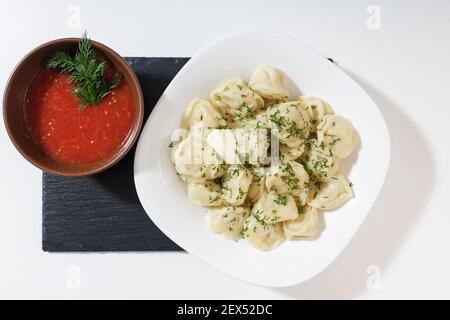 Hausgemachte Knödel in der Küche ohne Dekorationen. Fertige Knödel auf einem weißen Teller, serviert mit Adjika Stockfoto