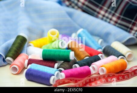 Set von bunten Nähfäden, Nahaufnahme. Stoff zum Nähen im Hintergrund. Stockfoto