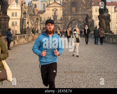 Prag, Tschechische Republik. 03-02-2021. Junger Mann, der im Winter auf der Karlsbrücke im Stadtzentrum von Prag mit einem wunderschönen Sonnenuntergang läuft. Stockfoto