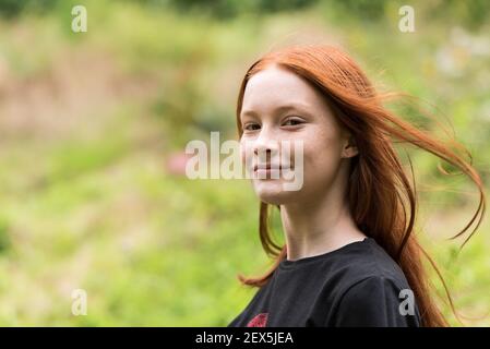 Rothaarige zwölf Jahre altes Mädchen mit Sommersprossen posiert mit Ein Natur Bokeh Hintergrund Stockfoto