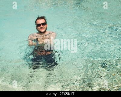 Der junge Erwachsene Mann trägt eine Sonnenbrille am Pool Stockfoto
