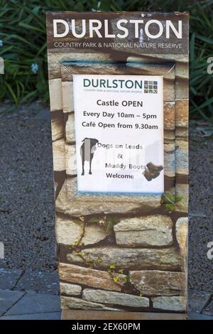 Begrüßungsschild und Öffnungszeiten für Durlston Castle im Durlston Country Park, Swanage, Dorset, UK im April - Hunde auf Leine und schlammige Stiefel willkommen Stockfoto