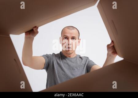 Staunender Mann Auspacken und Öffnen einer Karton-Geschenkbox und Blick nach innen. Ansicht aus der Box Stockfoto