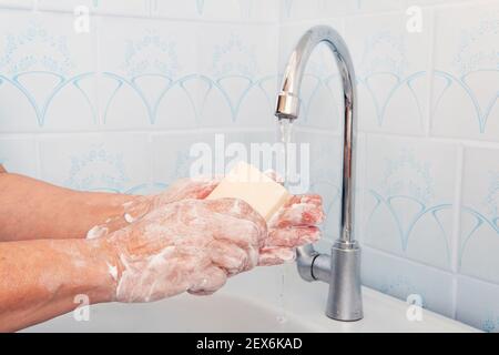 Eine Frau wäscht ihre Hände mit einem Stück weißer Seife in der Küche. Ältere ältere Frau seine Hände mit Seife unter Leitungswasser Wasserhahn. Hygiene Illustration Stockfoto