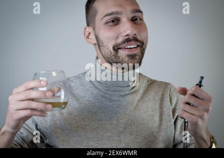 Porträt eines jungen bärtigen Mannes, der eine elektronische raucht Zigarette, die ein Glas Bier aus der Nähe hält Stockfoto