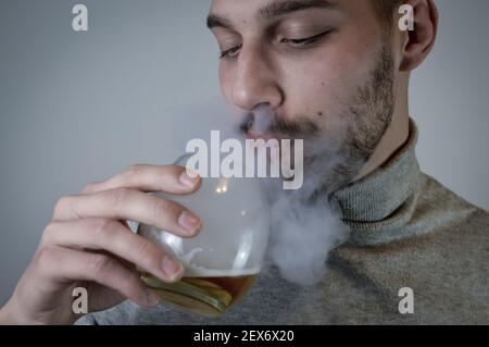 Porträt eines jungen bärtigen Mannes, der Rauch von einem ausatmet Elektronische Zigarette hält ein Glas Bier in der Nähe Stockfoto