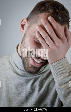 Porträt eines lächelnden jungen Mannes, der seine Stirn berührt Ein Moment der Verlegenheit Stockfoto