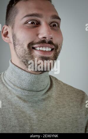 Porträt eines lächelnden jungen braunhaarigen Mannes mit einem kurzen Bart und ein grauer Rollkragenpullover Stockfoto