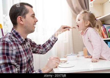 Fürsorglicher Vater füttert seine geliebte Tochter leckeres Essen mit einem Löffel. Stockfoto