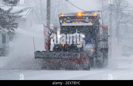 Ein städtischer Schneepflug schiebt Schnee während der Höhe eines Schneesturms in schrecklicher Sicht mit gelben Lichtern zu sehen. Stockfoto